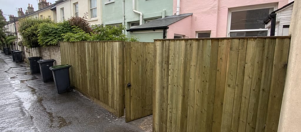Pastel rendered terrace backs in Bedminster, an alley gate set into the fence line and wheelie bins along the alley