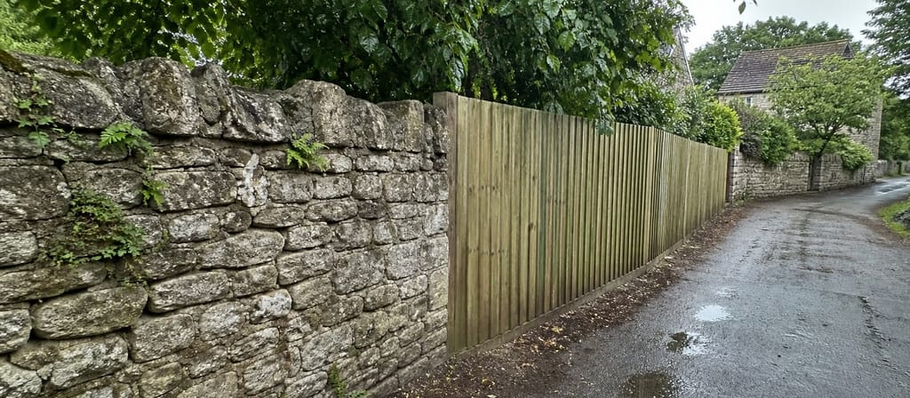 A limestone rubble wall running along a Westbury lane with a timber fence carrying the boundary on where the wall ends