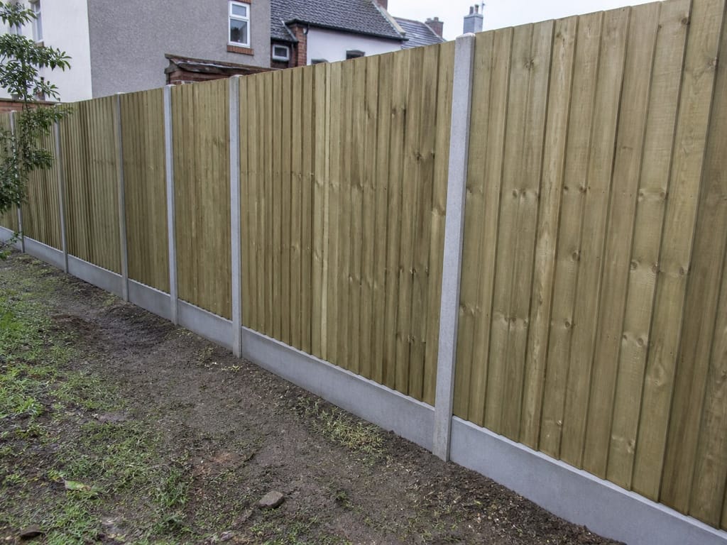 A closeboard run built on concrete posts with concrete gravel boards along the bottom, seen down the length of a damp garden boundary