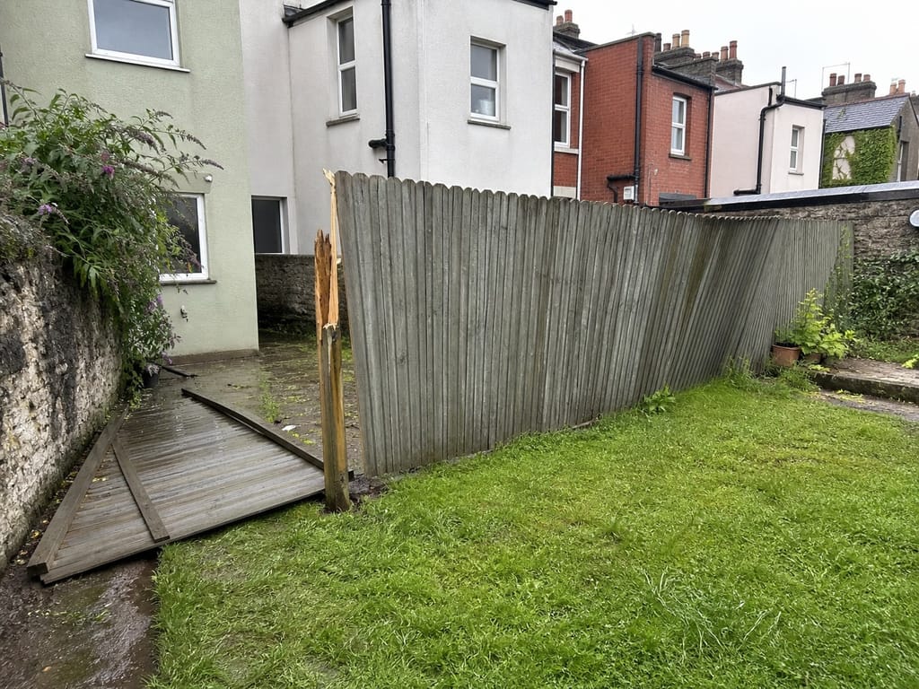 A storm damaged closeboard run on arrival, leaning across the lawn with one bay down and the broken post still in the ground
