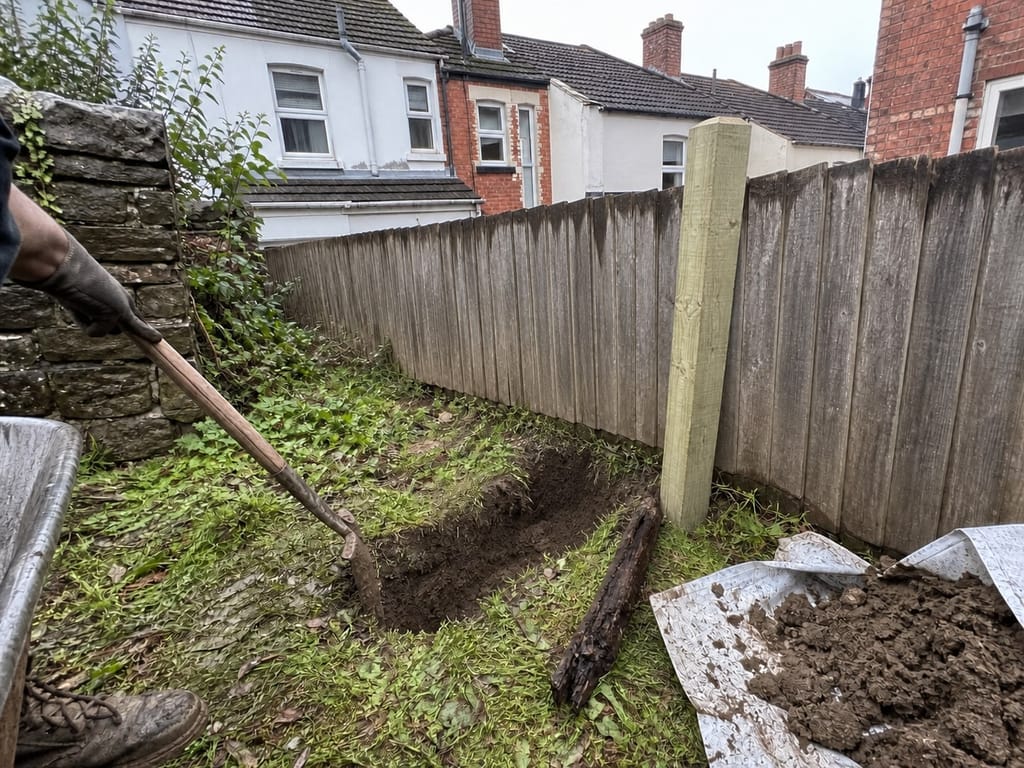 A snapped post dug out and the hole opened up, with the rotted stub on the grass beside the fresh replacement post