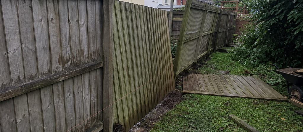 A storm-hit closeboard run in a Bristol terrace garden, two bays leaning well out of plumb with a section flat on the wet grass and a string line set for the repair